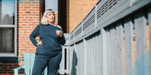 woman in sweatpants standing in an urban backyard holding coffee